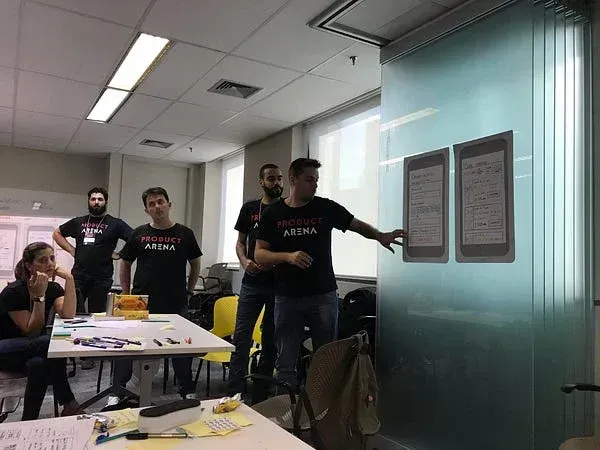 Horácio Soares apresentando para grupo em sala de treinamento, com whiteboard e tela projetando interface de aplicativo, participantes sentados em cadeiras amarelas.