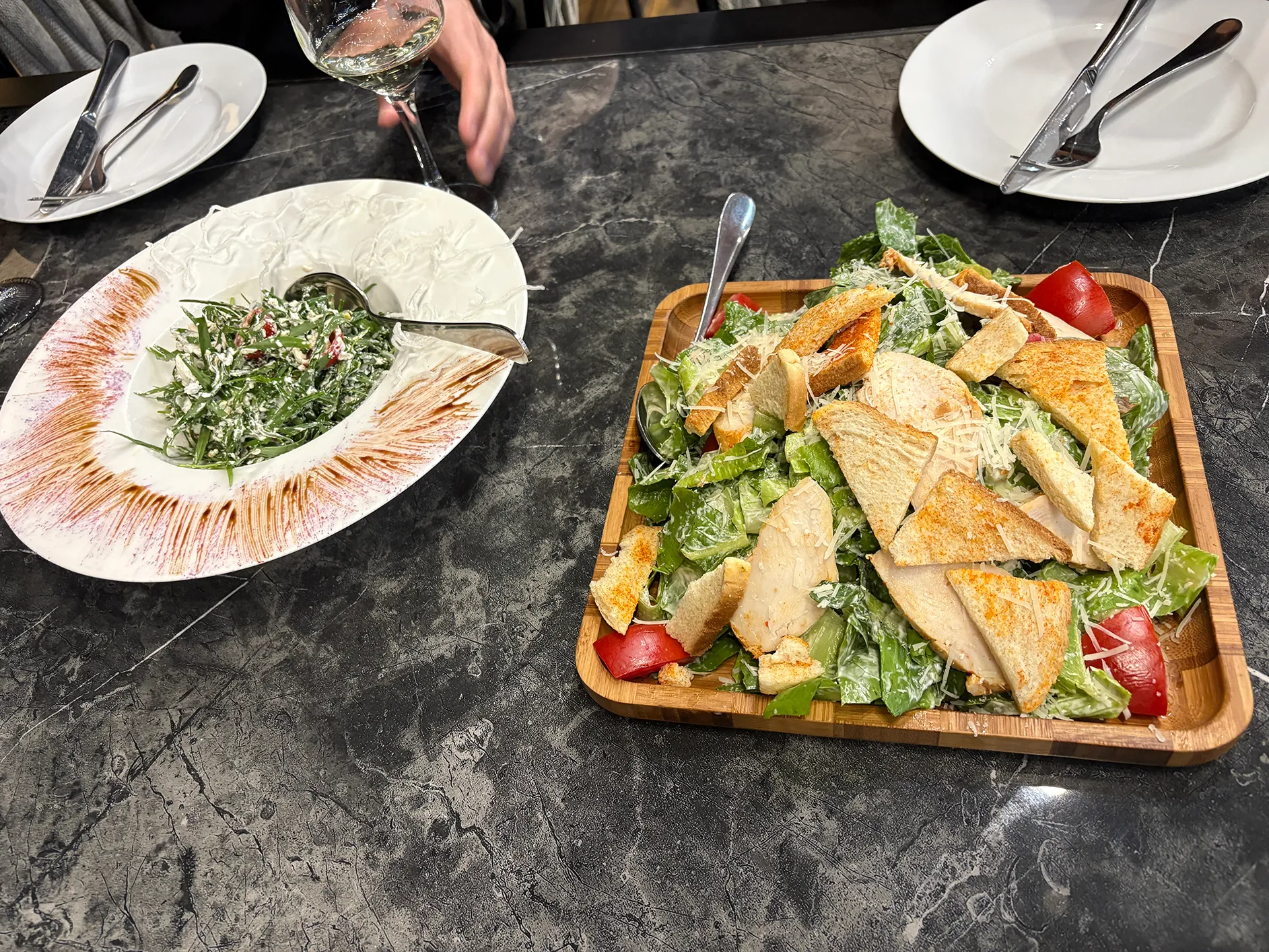 Dois pratos de saladas em cima da mesa, o primero era uma salada local com molho e a segunda era uma salada cesar.
